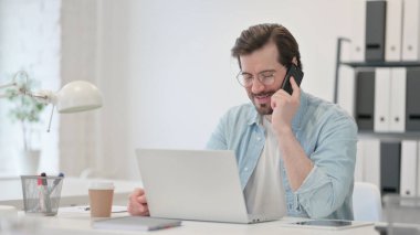 Dizüstü bilgisayarlı genç adam telefonda konuşuyor.
