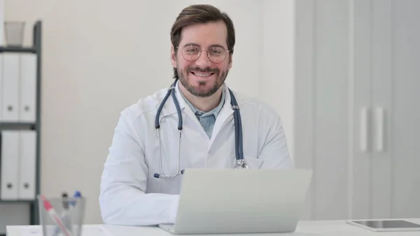 Молодой доктор с ноутбуком улыбается в камеру — стоковое фото