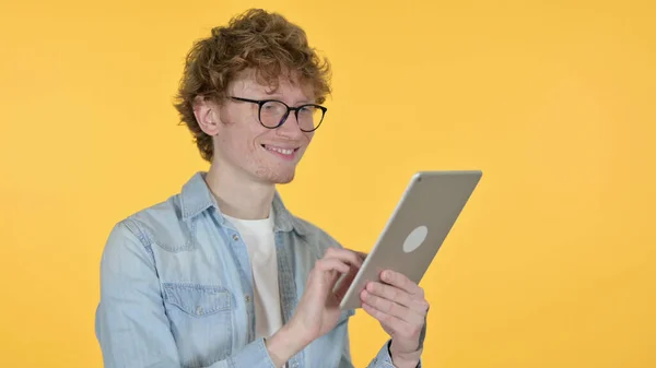 Rödhårig ung man med hjälp av digital tablett på gul bakgrund — Stockfoto