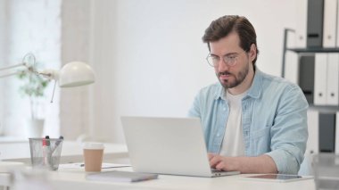 Ofiste dizüstü bilgisayarda çalışan genç adam.