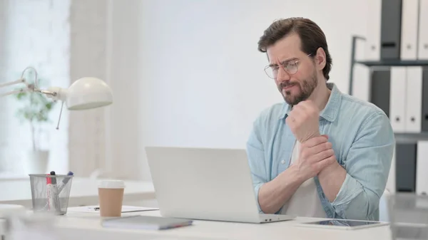 Junger Mann mit Handgelenkschmerzen arbeitet am Laptop — Stockfoto