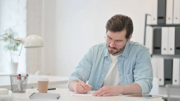 Junger Mann schreibt im Amt auf Papier — Stockfoto