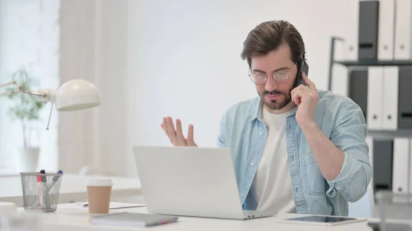 Wütender junger Mann mit Laptop telefoniert — Stockfoto