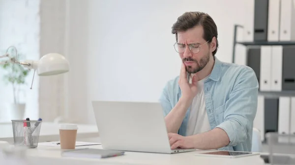 Mladý muž s bolestí zubů pracuje na notebooku — Stock fotografie