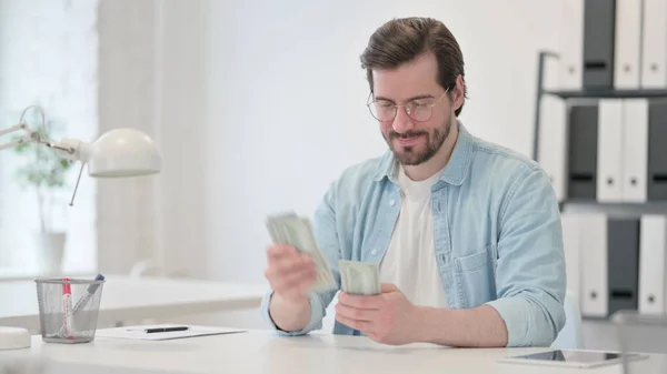 Счастливый молодой человек считает доллары на работе — стоковое фото