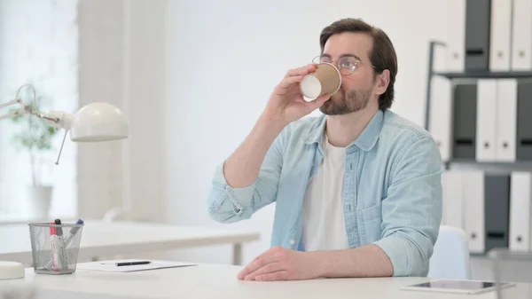 Entspannter junger Mann trinkt Kaffee bei der Arbeit — Stockfoto