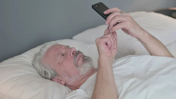 Unavený starý muž pomocí Smartphone v posteli — Stock fotografie