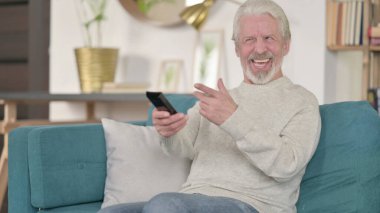 Heyecanlı yaşlı adam evde televizyon izliyor.