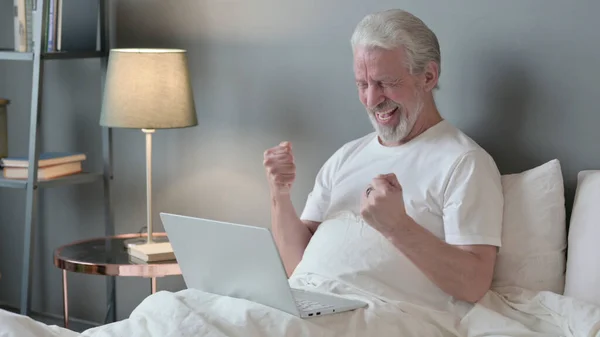 Succesvolle senior oude man met laptop viert feest in bed — Stockfoto