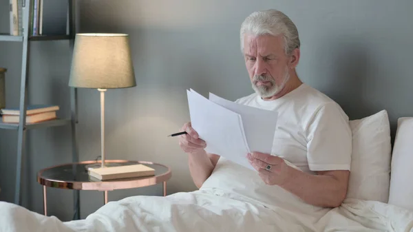Starszy człowiek Czytanie dokumentów w łóżku — Zdjęcie stockowe