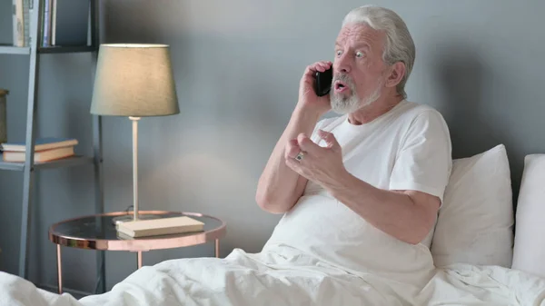 Angry Senior Old Man Talking on Phone in Bed