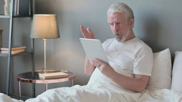 Anciano mayor reaccionando a la pérdida en la tableta en la cama — Foto de Stock