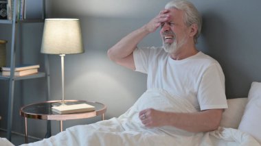 Baş ağrısı olan yaşlı bunak. Yatakta oturuyor.