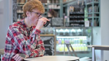 Kafede su içen kızıl saçlı genç adam.