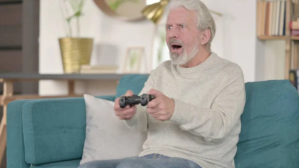 Старший старик празднует успех в видеоигре дома — стоковое фото