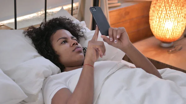 Smartphone χρήση από νεαρή αφρικανική γυναίκα ξαπλωμένη στο κρεβάτι — Φωτογραφία Αρχείου