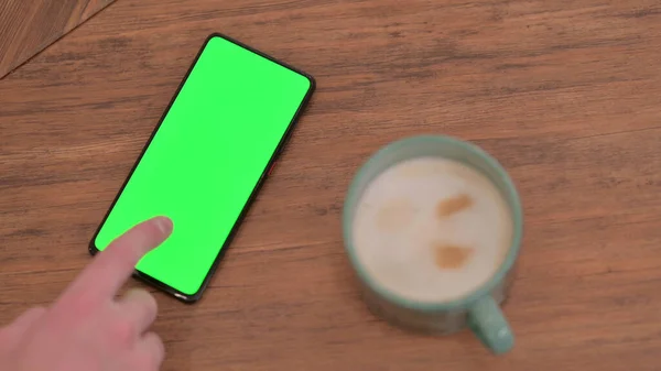 Dedo haciendo clic en la pantalla verde Smartphone en la mesa —  Fotos de Stock