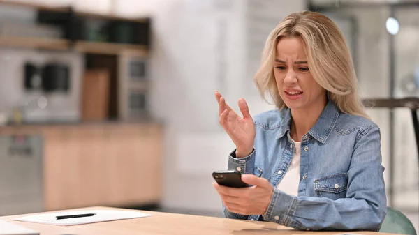 Mujer Casual joven infeliz con pérdida en el teléfono inteligente en el trabajo —  Fotos de Stock