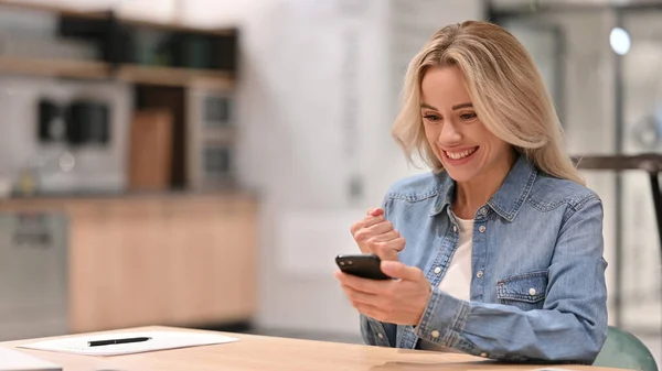 Junge Gelegenheitsfrau, die bei der Arbeit mit dem Smartphone jubelt, Erfolg — Stockfoto