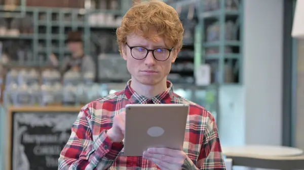 Portrait de sérieux jeune rousse jeune homme à l'aide de tablette numérique — Photo