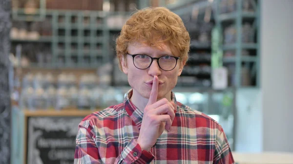 Portret van de jonge roodharige jongeman met vinger op de lippen, Stil gebaar — Stockfoto