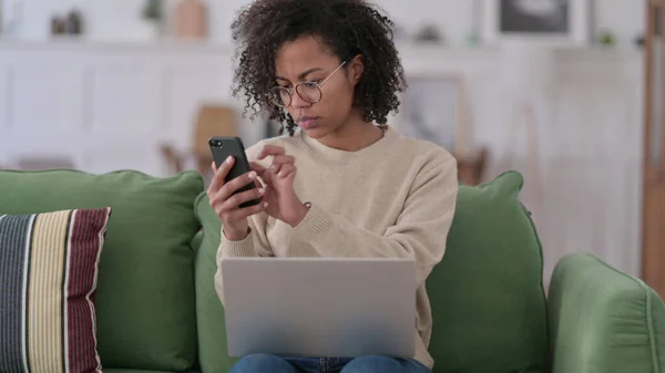 自宅でスマートフォンやノートパソコンで働く若いアフリカ人女性 — ストック写真