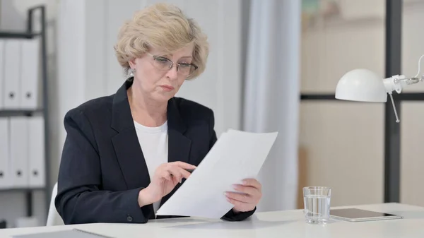 Alte Geschäftsfrau liest Dokumente bei der Arbeit — Stockfoto