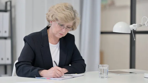 Vieille femme d'affaires écrivant sur le papier au travail — Photo