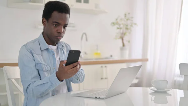 Afričan pracuje na smartphonu a notebooku doma — Stock fotografie