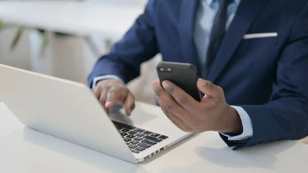 Primo piano di uomo d'affari africano utilizzando Smartphone e laptop — Foto Stock