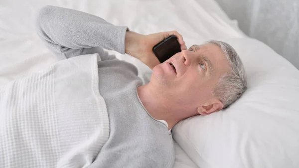 Pozytywny staruszek rozmawiający przez telefon w łóżku — Zdjęcie stockowe