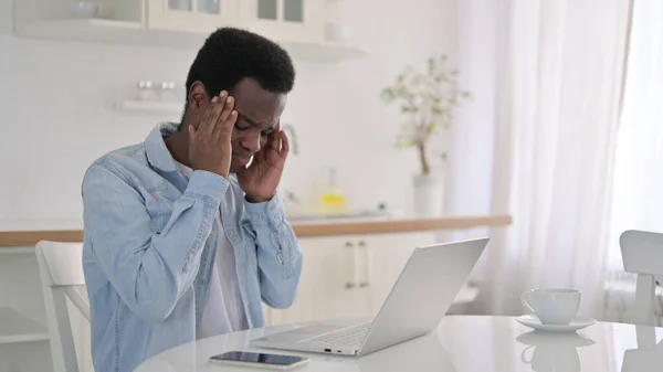 Unavený africký muž s notebookem s bolestí hlavy doma — Stock fotografie