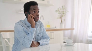 Evde akıllı telefondan konuşan neşeli Afrikalı adam.