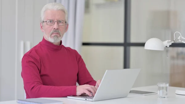 Oude man op zoek naar Camera tijdens het gebruik van Laptop — Stockfoto