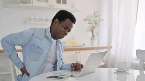 Afričan muž s notebookem s bolestí zad doma — Stock fotografie