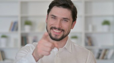 Neşeli genç adam kamerayı işaret ediyor.