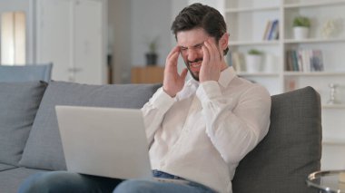 Bilgisayarlı yorgun genç adam evde baş ağrısı çekiyor. 