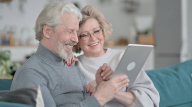 Koltukta oturup tablet kullanan mutlu yaşlı çift.