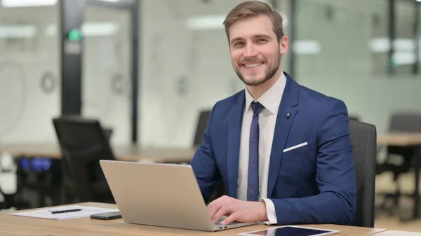 Empresario con portátil sonriendo a la cámara — Foto de Stock