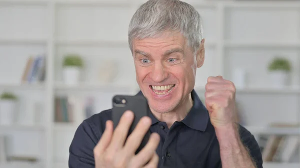 Чоловік середнього віку святкує успіх на смартфоні — стокове фото