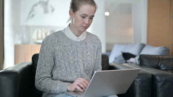 Mujer seria sentada en un sofá y trabajando en un ordenador portátil — Foto de Stock
