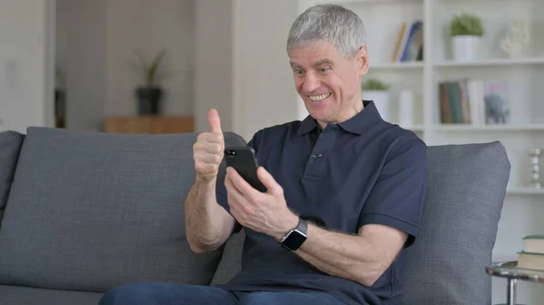 Hombre de mediana edad celebrando el éxito en el teléfono inteligente en el sofá —  Fotos de Stock