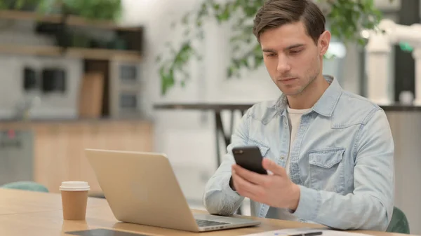 Young Man with Laptop using Smartphone at Work — Stock Photo, Image