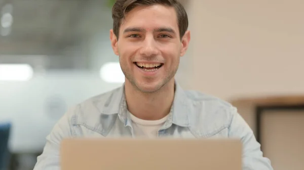 Primer plano de hombre joven con el ordenador portátil sonriendo a la cámara — Foto de Stock