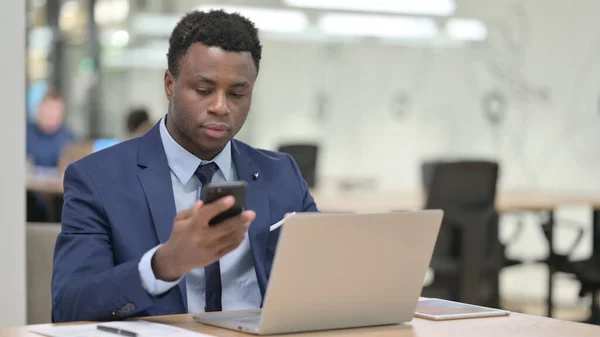 非洲商人在笔记本电脑上工作时使用智能手机 — 图库照片