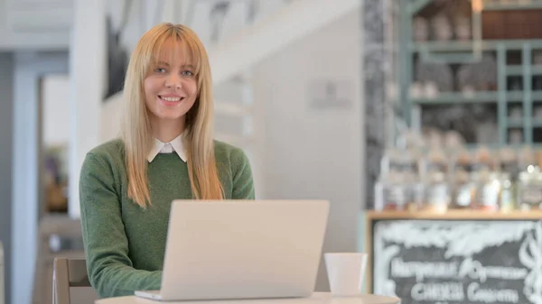Mulher sorrindo para a câmera enquanto trabalhava no laptop no café — Fotografia de Stock