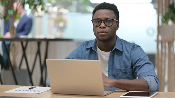 Africain homme regardant caméra tout en travaillant sur ordinateur portable — Photo