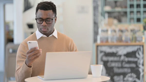African Man pomocí Smartphone při práci na notebooku — Stock fotografie