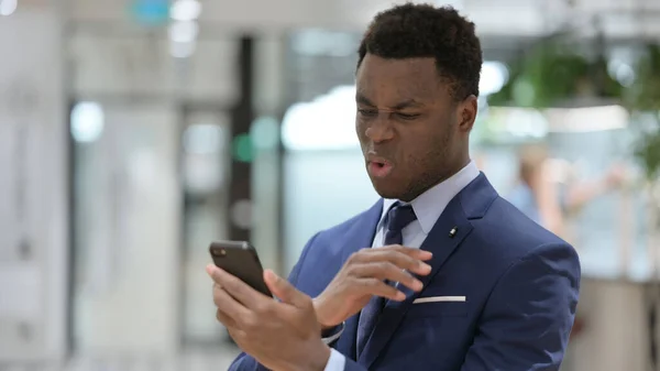 Africano Empresário perturbado pela perda no Smartphone — Fotografia de Stock