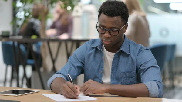 Afrikansk man skriver på papper i moderna kontoret — Stockfoto